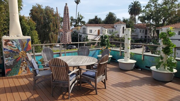 A wooden deck with a round table and chairs, surrounded by potted plants and a mosaic wall. - An Unbeatable Location with Historic Character (Santa Barbara)
