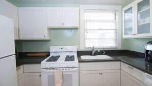 A kitchen with white cabinets, a stove, a sink, and a window with blinds. - An Unbeatable Location with Historic Character (Santa Barbara)