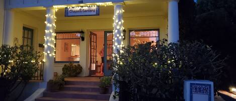 A building entrance with a sign reading "Chapaí Gardens" and a number "118" above the door. There are steps leading up to the entrance, and the area is decorated with string lights.