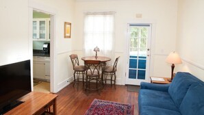 A living room with a blue sofa, a wooden coffee table, a dining table with four chairs, a TV, and a kitchen visible through an open door. - An Unbeatable Location with Historic Character (Santa Barbara)