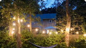 A hammock strung between trees in a backyard with a house in the background.