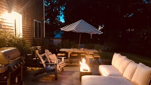 An outdoor patio with a grill, chairs, a table, a striped umbrella, and a sofa.