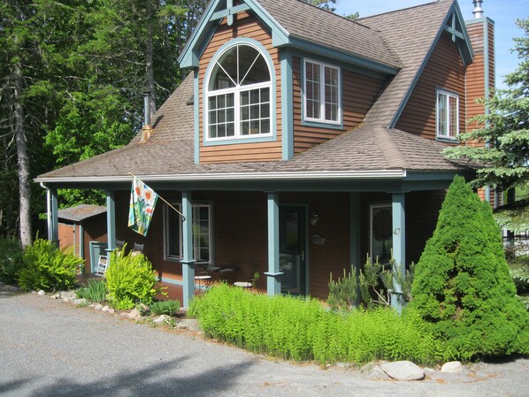 A two-story wooden house with a porch, a chimney, and a flag.