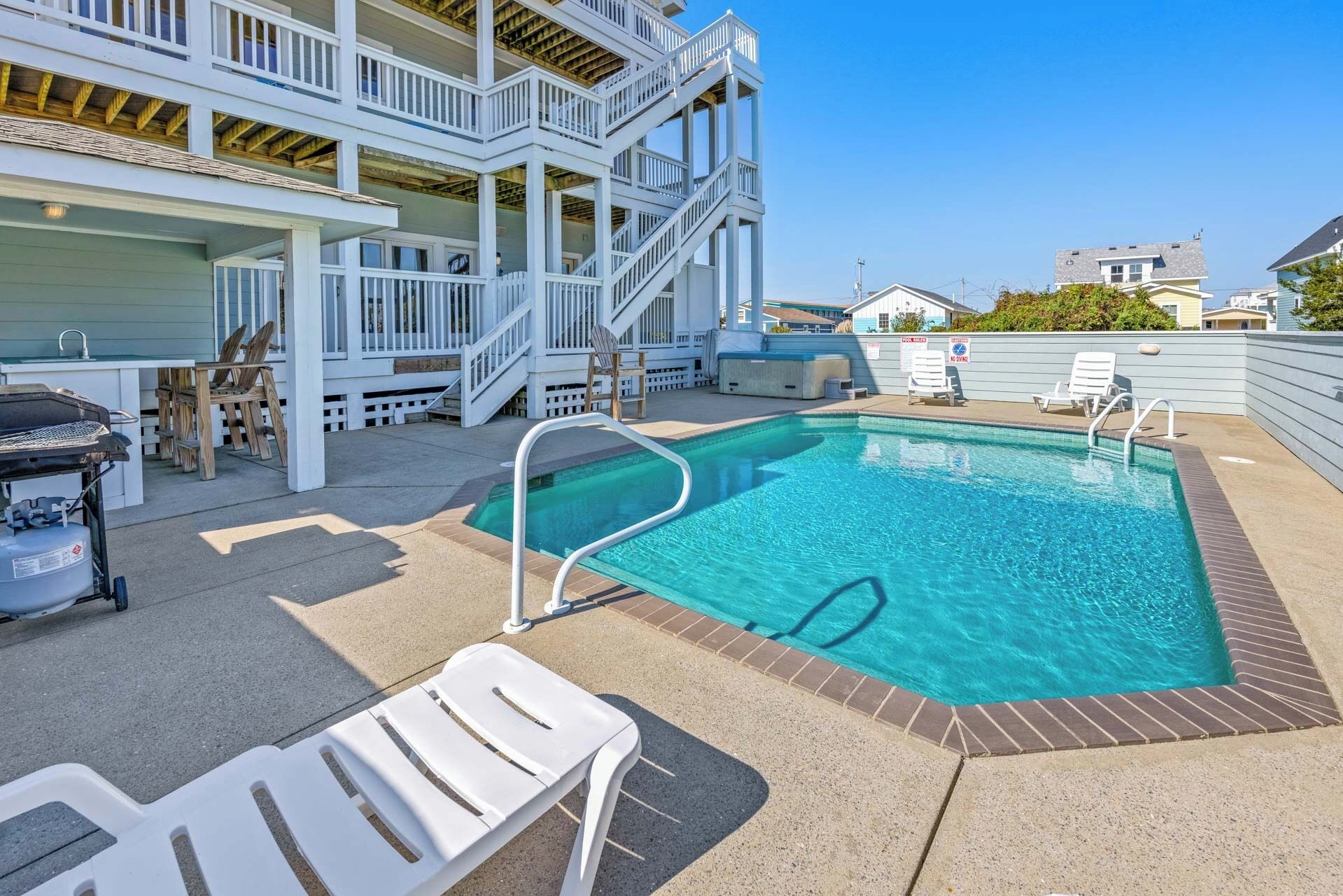A swimming pool with a wooden deck, white lounge chairs, and a barbecue grill.