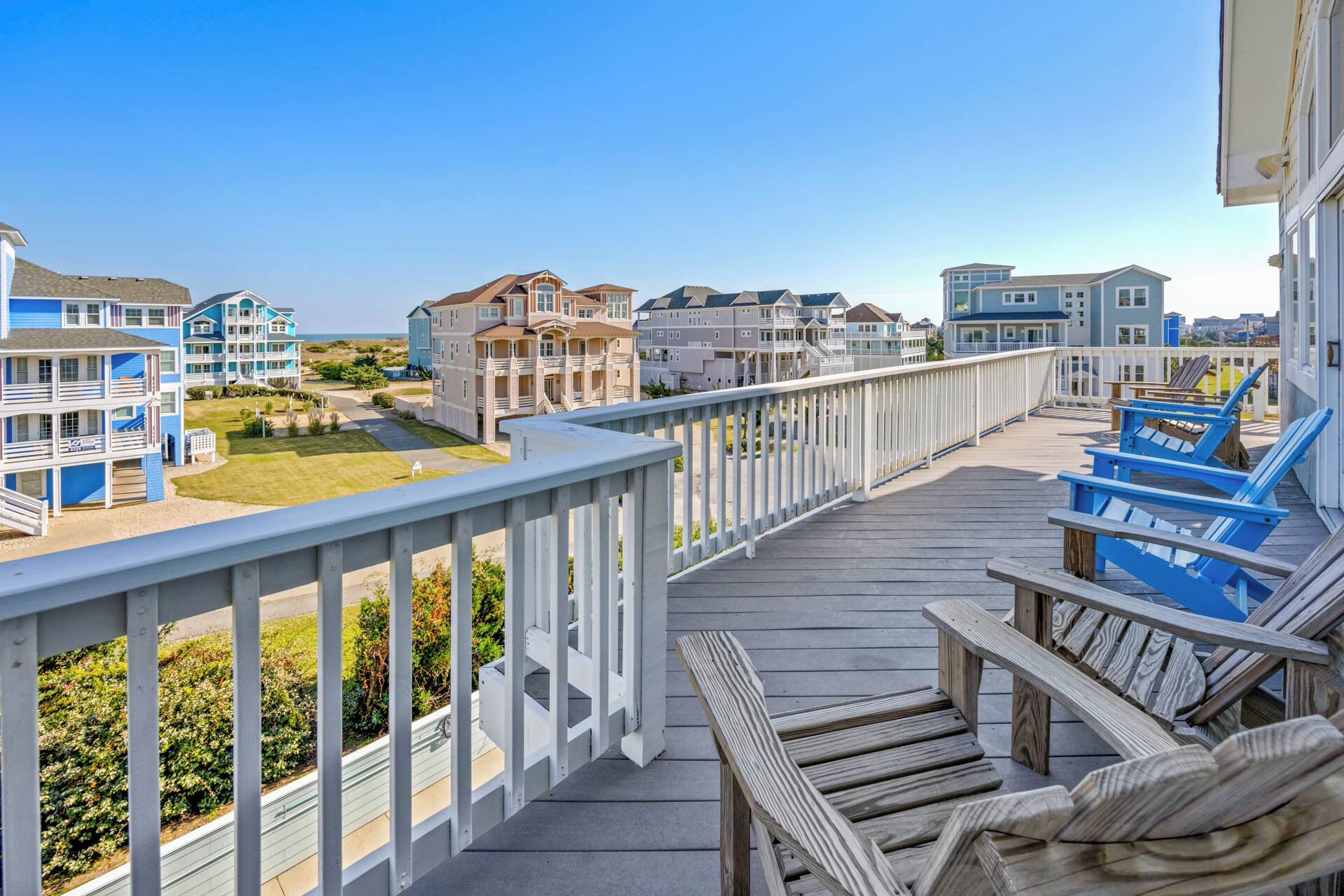 A wooden deck with blue lounge chairs, overlooking a beachfront with multi-story buildings.
