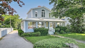 Ein zweistöckiges Haus mit einer Veranda, einem Vorgarten mit Rasen und einem Weg zum Haus.
