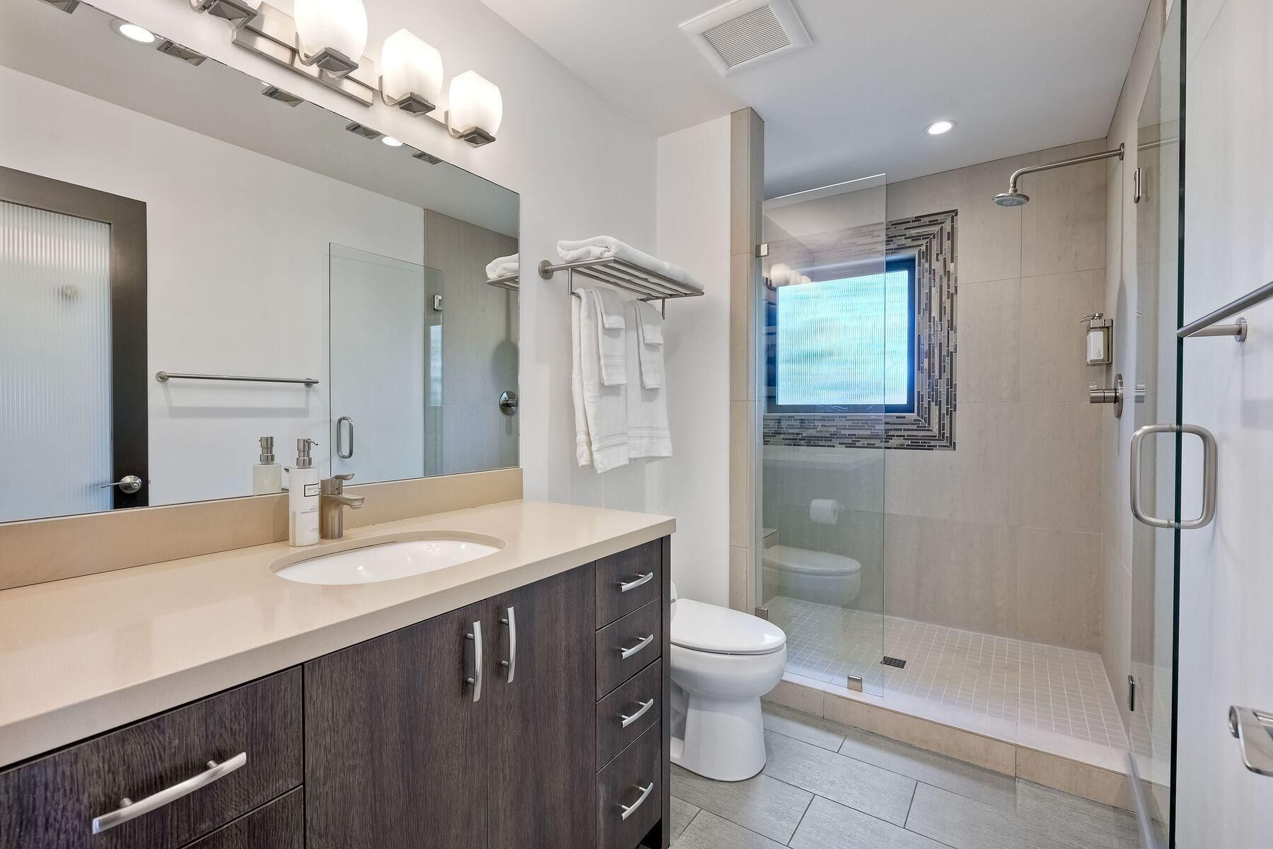 Un baño moderno con dos lavamanos, un espejo grande y cabina de ducha con paredes de vidrio.