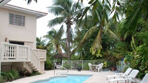 Una piscina con sillas de descanso, una escalera que lleva a un balcón y palmeras que la rodean.