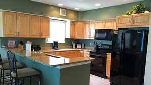 Una cocina moderna con encimeras de granito, armarios de madera, un refrigerador negro y un horno empotrado.