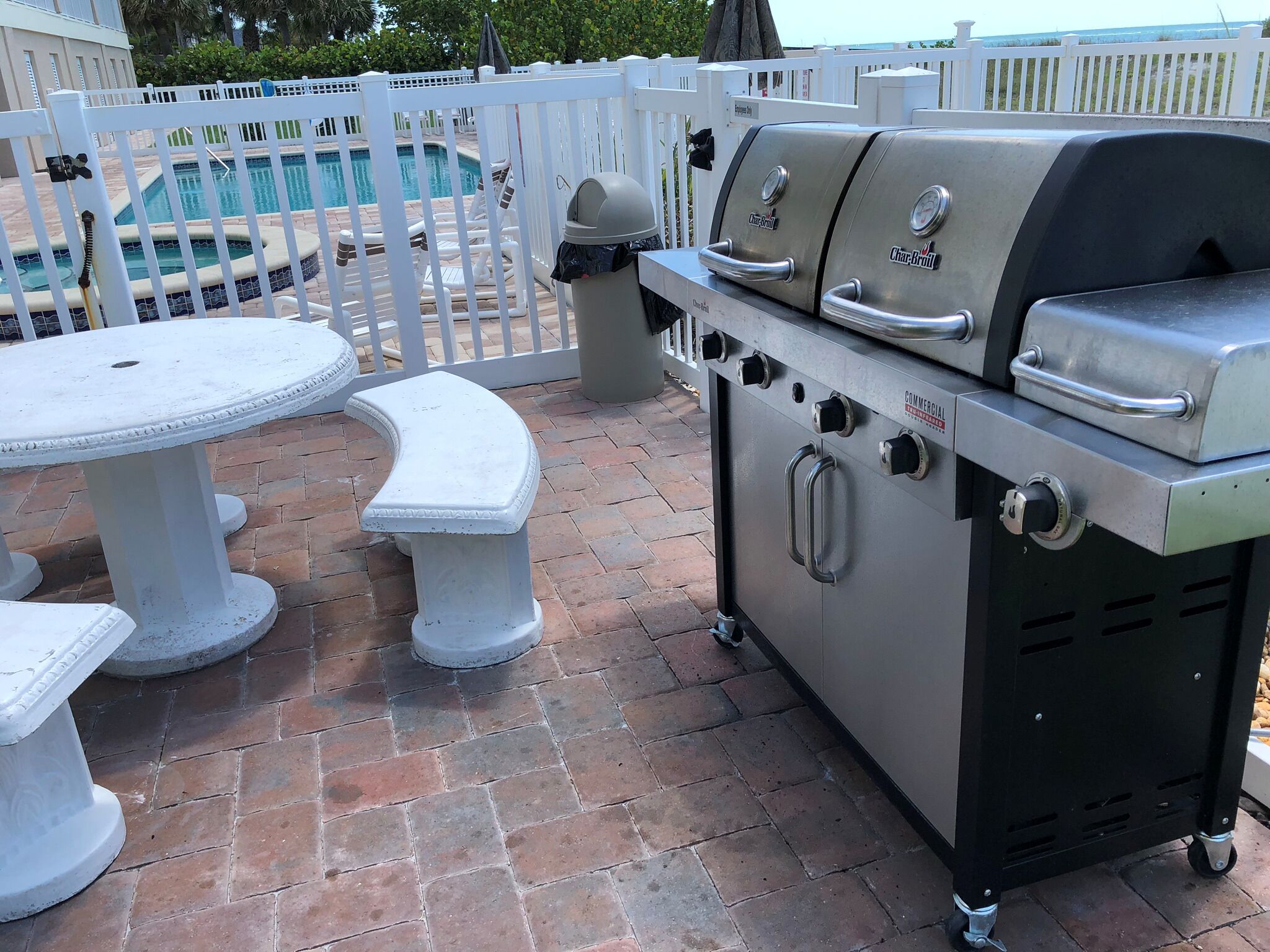 An outdoor patio with a barbecue grill, a pool, and a white fence.