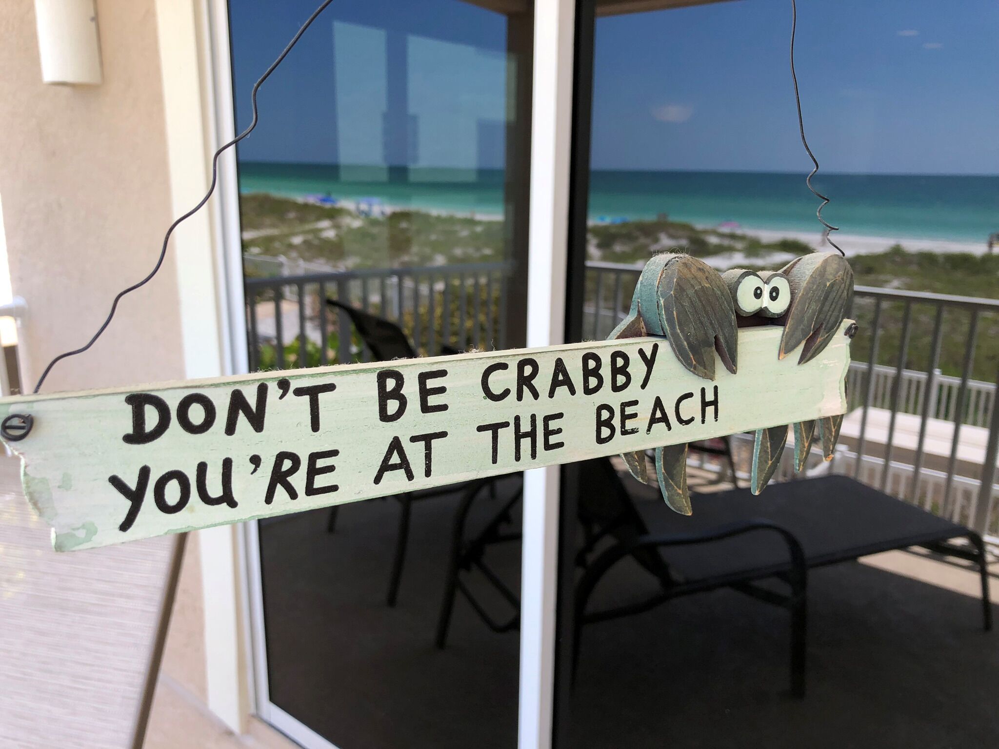 Un letrero con un búho y el texto 'DON'T BE CRABBY YOU'RE AT THE BEACH' colgado de la barandilla de un balcón.