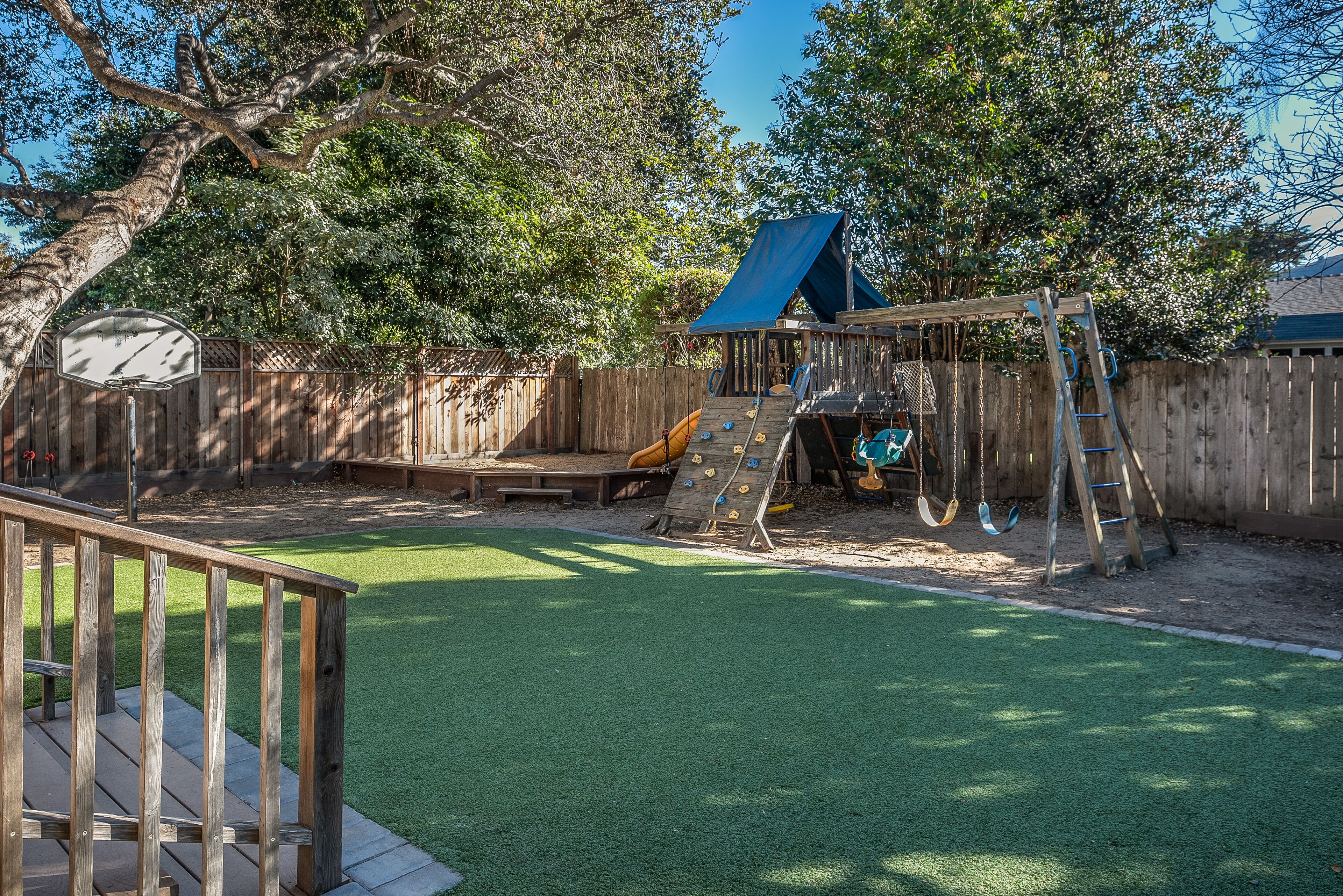 A backyard with a wooden deck, a swing set, and a slide.