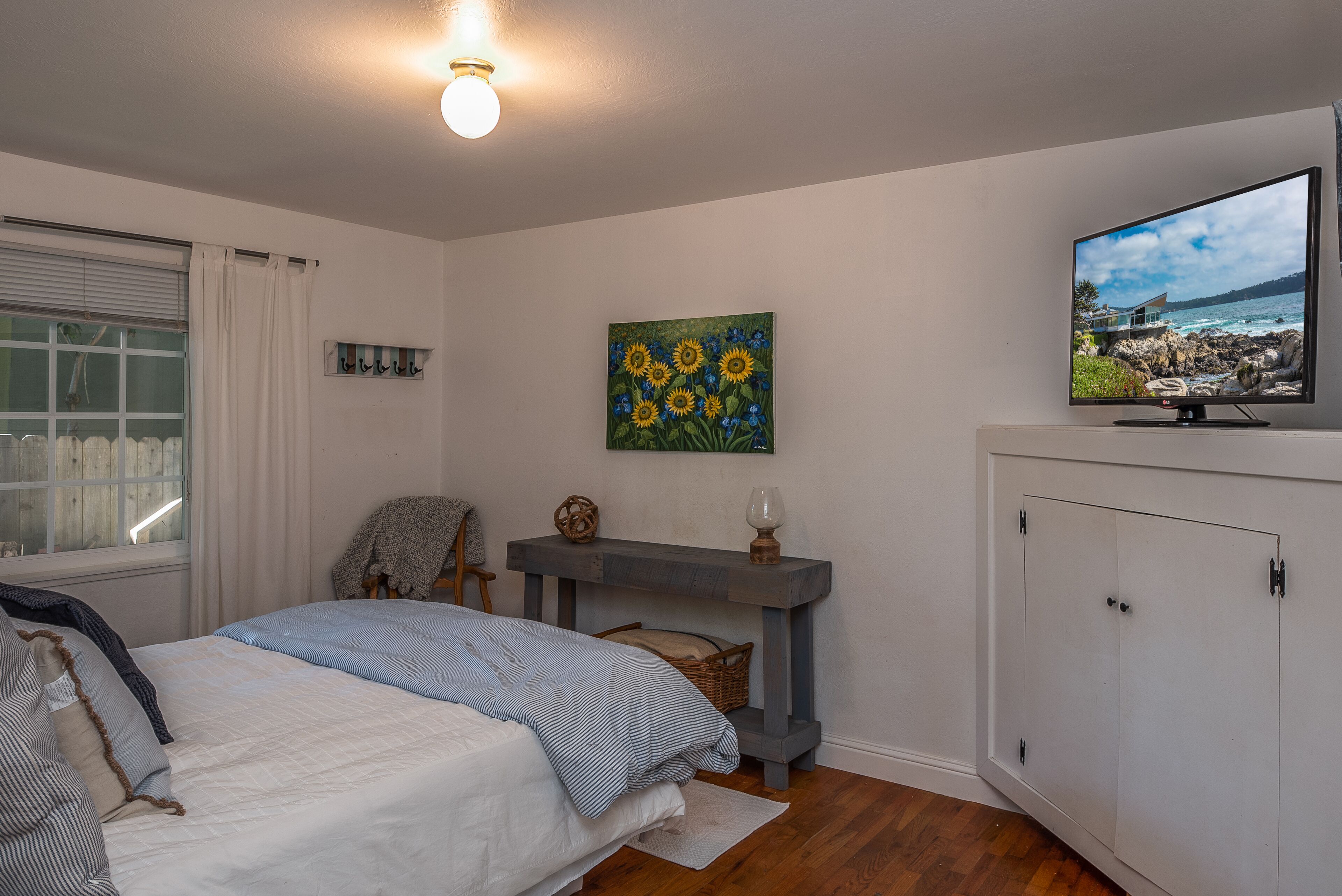 A bedroom with a bed, a painting, a television, and a wardrobe.