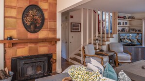 A cozy living room with a fireplace, comfortable seating, and a staircase leading to another level.