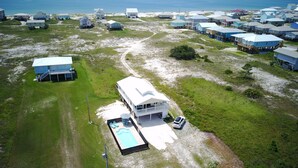 An aerial view of a coastal residential area with houses on stilts, a swimming pool, and a clear view of the ocean. - Book now for Fall 2026! Pet friendly! (Gulf Shores)
