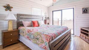 A bedroom with a wooden bed, a nightstand with a lamp, a dresser, and a balcony with a view. - Book now for Fall 2026! Pet friendly! (Gulf Shores)