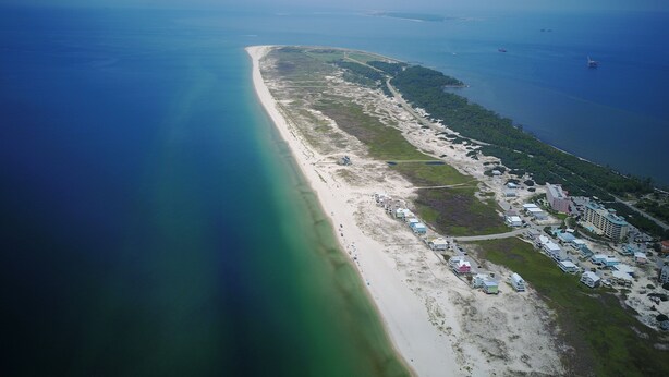 An aerial view of a coastal area with a long sandy beach, a marina with boats, and a resort with multiple buildings along the shore. - Book now for Fall 2026! Pet friendly! (Gulf Shores)