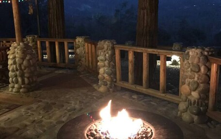An outdoor patio area with a stone fire pit, wooden deck, and a covered seating area with string lights.