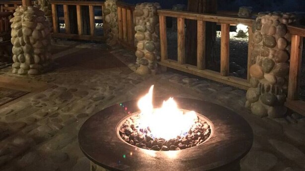 An outdoor patio area with a stone fire pit, wooden deck, and a covered seating area with string lights. - Yosemite! Dogs & family! Mountain Air, come visit and make Wonderful Memories! (Oakhurst)