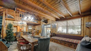 A rustic cabin interior with a wooden dining table, chairs, a bench, a Christmas tree, and a large window with blinds. - Yosemite! Dogs & family! Mountain Air, come visit and make Wonderful Memories! (Oakhurst)