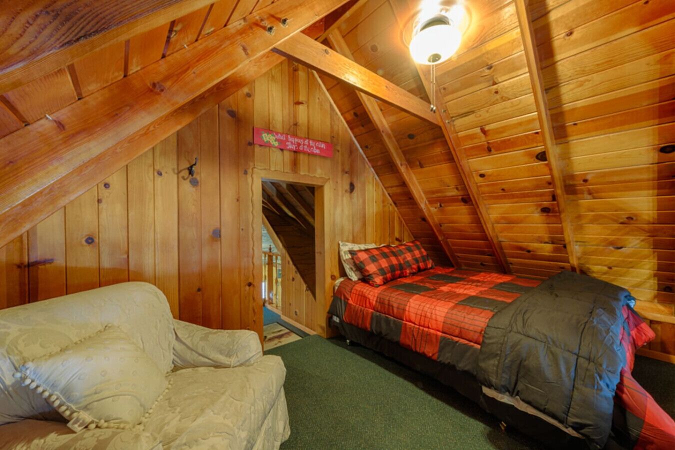 Um quarto de sótão aconchegante, com teto inclinado, uma cama com cobertor xadrez vermelho e preto, e uma cadeira.