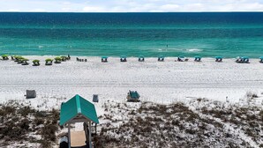 A beach with rows of beach chairs and umbrellas, a gazebo, and a sandy path leading to the water.