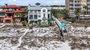 A beachfront property with a prominent staircase leading to a covered area, surrounded by palm trees and a sandy beach.
