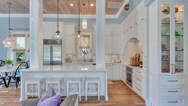 A spacious kitchen with white cabinetry, a central island with bar stools, and a dining area with a table and chairs.