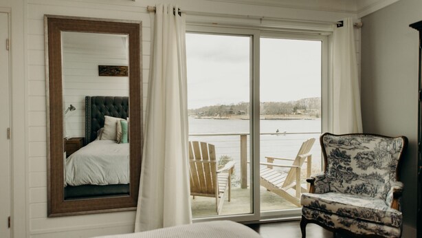 Une chambre avec une grande fenêtre, un lit, une chaise et une vue sur une étendue d’eau.