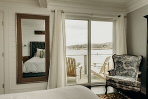 A bedroom with a large window, a bed, a chair, and a view of a body of water. - Waterfront Cottage in Branford (branford)