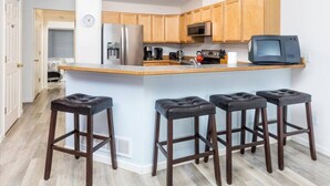 Una cocina moderna con armarios de madera, un refrigerador de acero inoxidable, un microondas y una isla grande con taburetes de bar.
