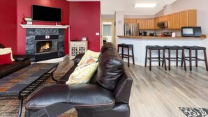 Una sala de estar moderna con chimenea, sofá de cuero y una zona de cocina con armarios de madera y un taburete de bar.