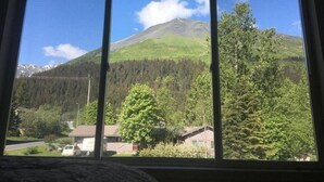 Vista desde una ventana de una montaña, con una zona boscosa y casas en primer plano.