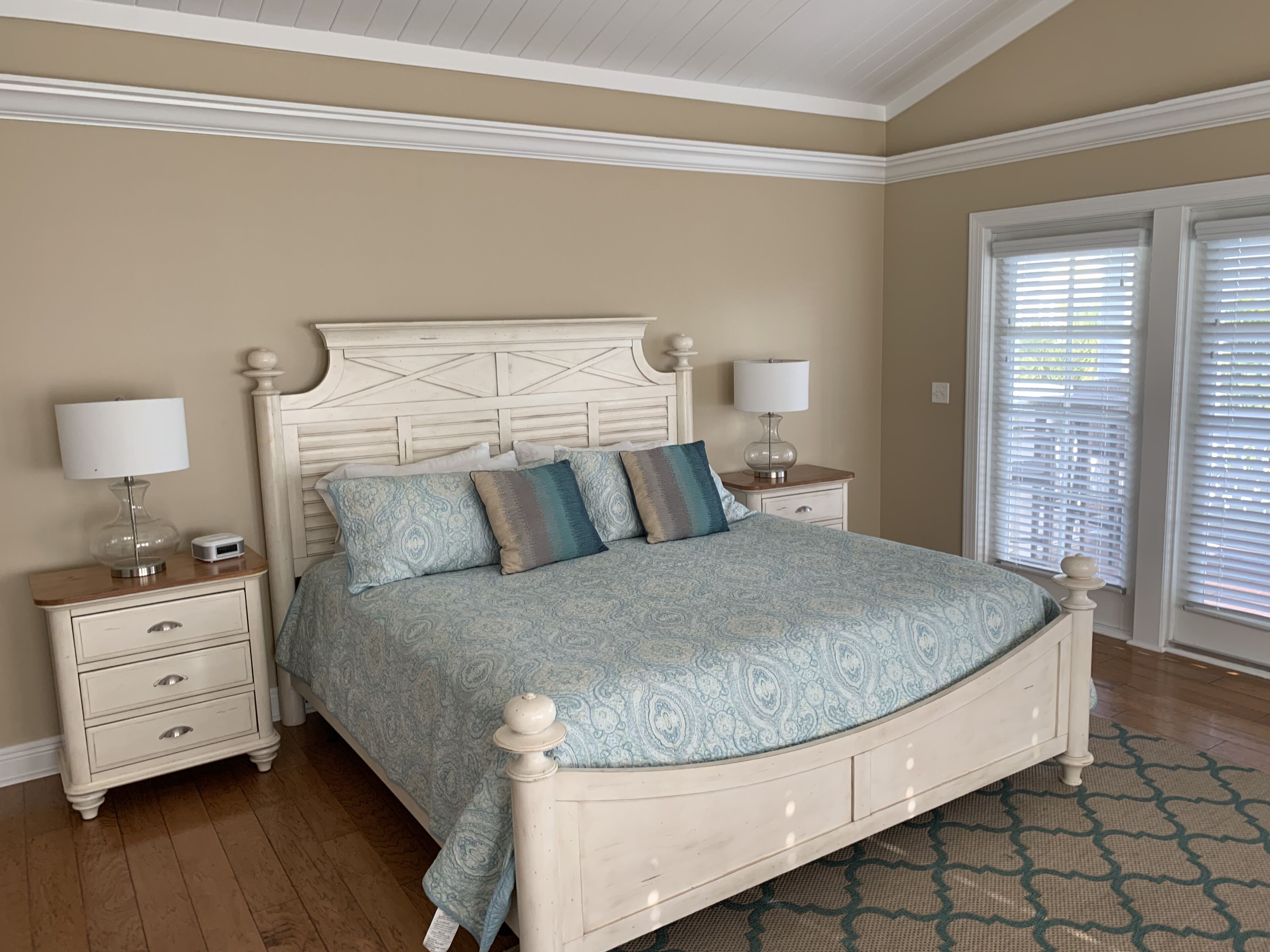 A bedroom with a large bed, two bedside tables, a nightstand, and a door with blinds.