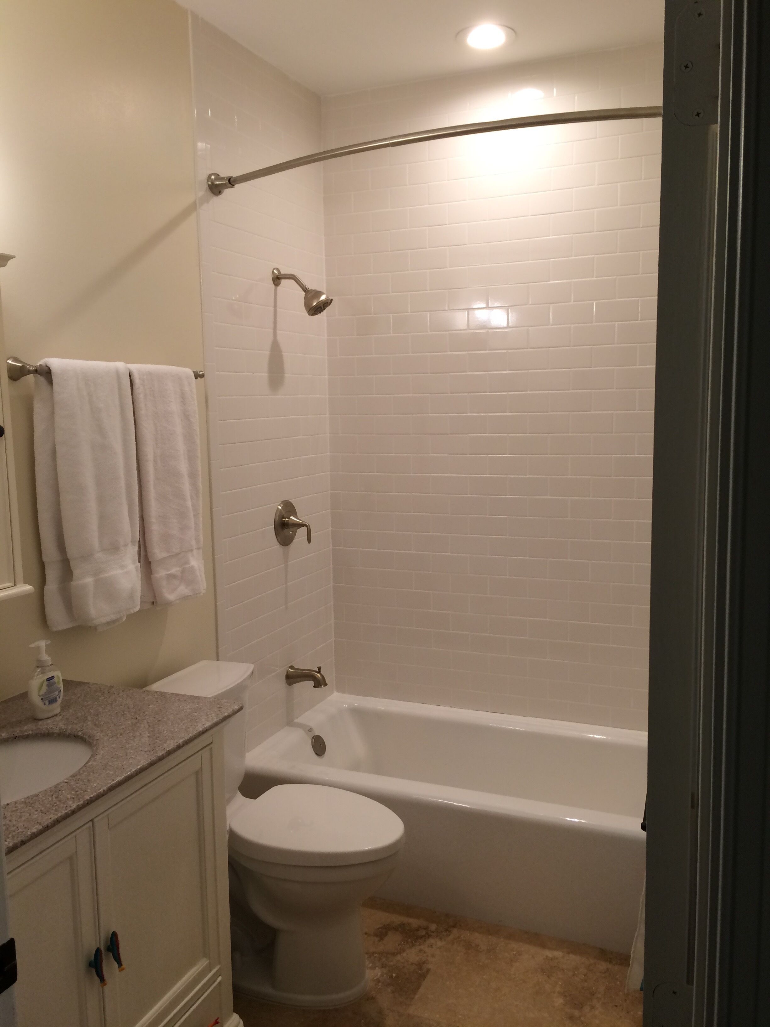 Een badkamer met een wit toilet, een wastafel met zeepdispenser, een badkuip en een douche met een gebogen glazen deur.