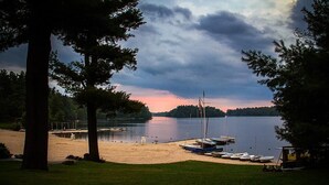 A lakeside beach with boats docked, a sandy shore, and a cloudy sky. - LAKESIDE ON LAKE NAOMI - boats, hot tub, beach, dock. Dogs OK (Pocono Pines)