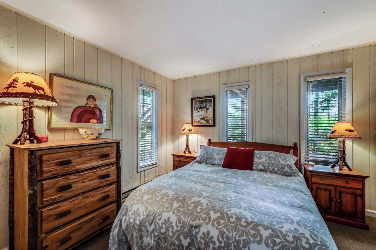 Un dormitorio con una cama grande, cómoda de madera, dos mesitas de noche y una ventana con persianas.