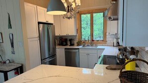 A kitchen with a marble countertop, stainless steel appliances, and a window with a view of trees. - LAKESIDE ON LAKE NAOMI - boats, hot tub, beach, dock. Dogs OK (Pocono Pines)