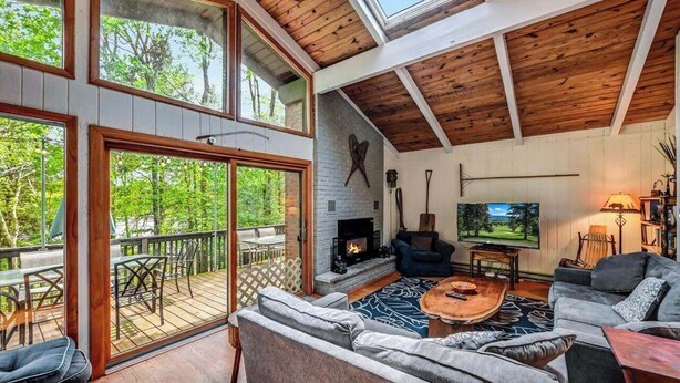 A spacious living room with a fireplace, large windows, and a balcony. - LAKESIDE ON LAKE NAOMI - boats, hot tub, beach, dock. Dogs OK (Pocono Pines)