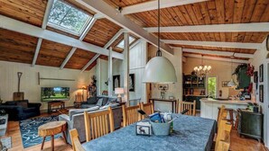 A spacious living area with a high ceiling, wooden beams, and a large dining table. - LAKESIDE ON LAKE NAOMI - boats, hot tub, beach, dock. Dogs OK (Pocono Pines)