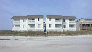 Ein Gebäude direkt am Strand mit mehreren Balkonen und einer flachen Dachterrasse.