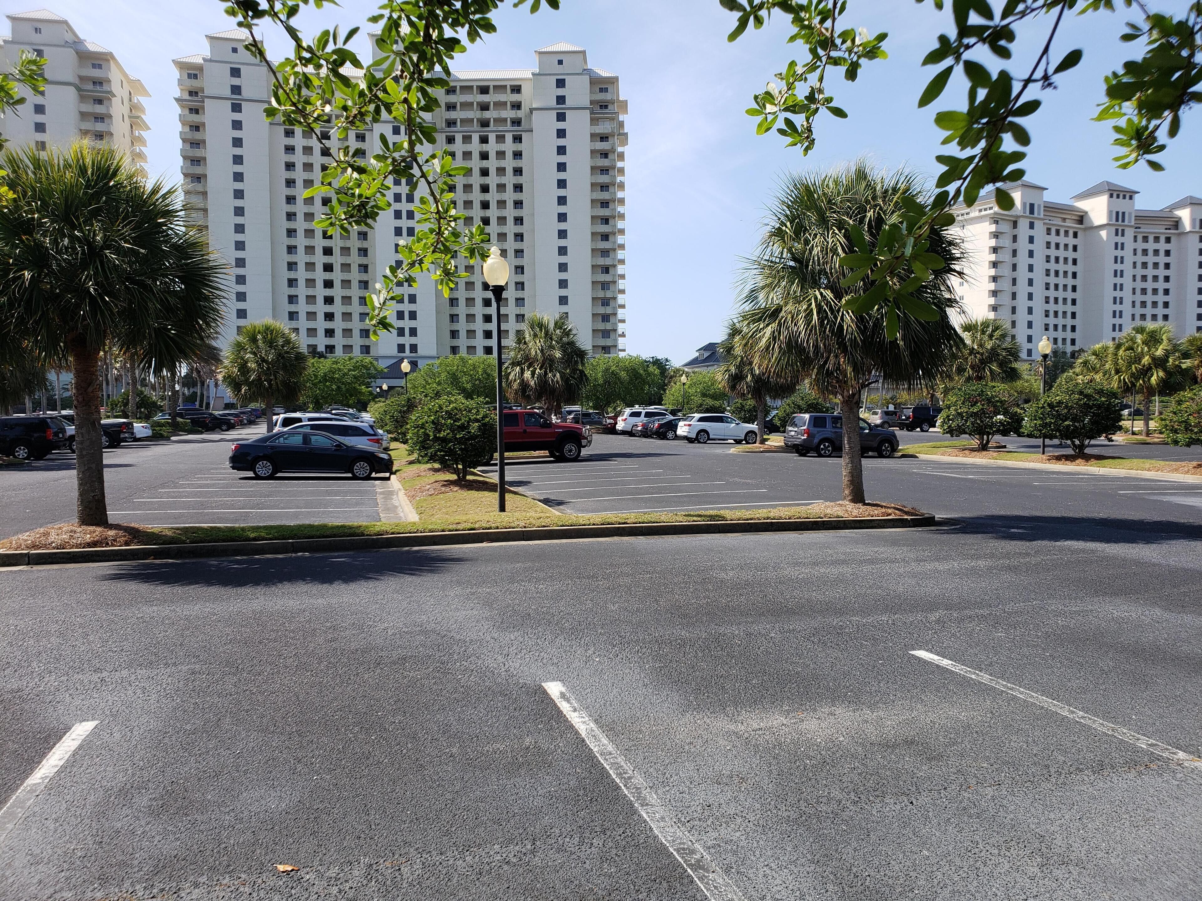 A parking lot with multiple cars, palm trees, and high-rise buildings in the background.