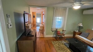 Una sala de estar con piso de madera, un sofá, un televisor y un comedor al fondo.
