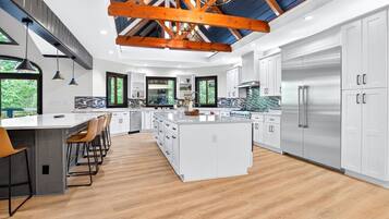 Une cuisine moderne dotée d’un grand îlot central, de meubles blancs, d’appareils électroménagers en acier inoxydable et d’un plafond en voûte.