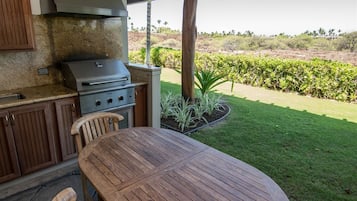 An outdoor kitchen with a grill, wooden cabinets, and a table.