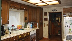 Una cocina con armarios de madera, un ventanal con persianas, un refrigerador y diversos electrodomésticos.