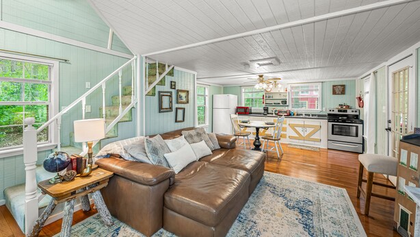 A spacious living room with a brown leather sofa, a wooden coffee table, and a staircase leading to an upper level. - Forget-Me-Knot Cottage at The Wilderness of Mentone adjoins the LRCNP (Mentone)