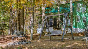 A rustic wooden swing set in a forested area with a green building in the background. - Forget-Me-Knot Cottage at The Wilderness of Mentone adjoins the LRCNP (Mentone)