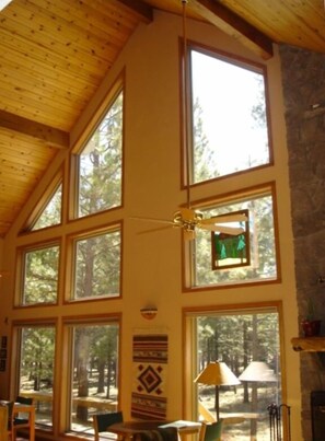 A cabin interior with large windows, wooden beams, and a stone wall. - Black Butte Ranch Mountain Style Home (Black Butte Ranch)