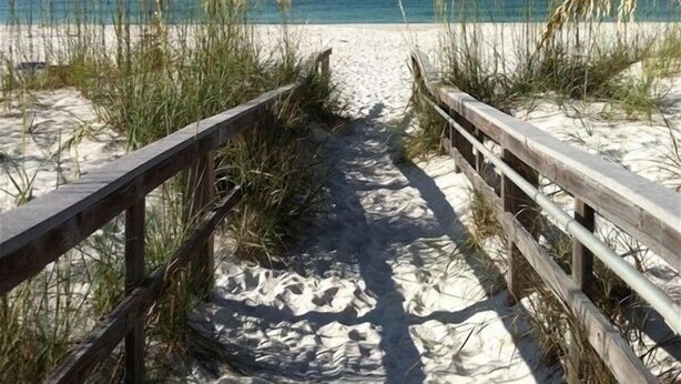 Ein Sandweg am Strand mit Holzgeländern, der zum Meer führt.